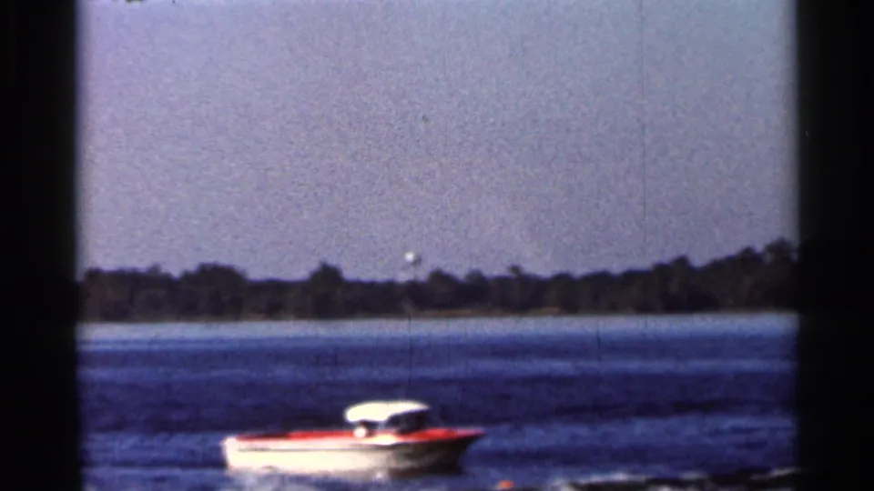 Small tow boat crossing a Florida lake in 1966 home-movie footage, with a dark tree line in the distance.