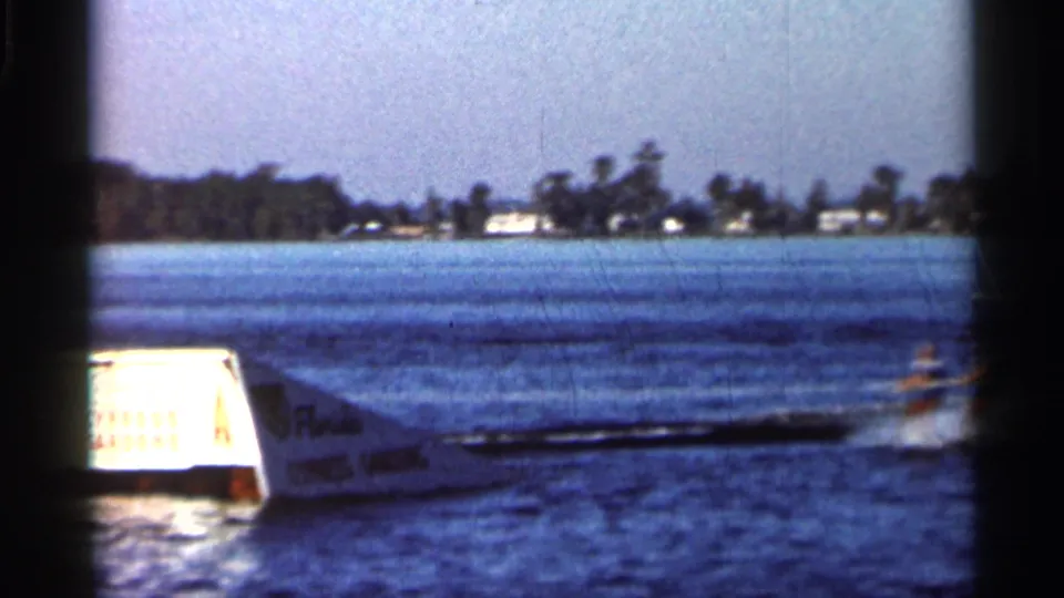 1966 Florida 8mm frame with a white motorboat moving beside a Cypress Lakes-marked ramp on open lake water.