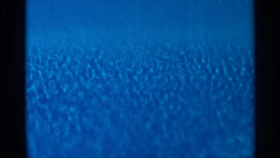 Saturated blue 8mm footage with visible grain and dark borders, continuing the abstract transition.