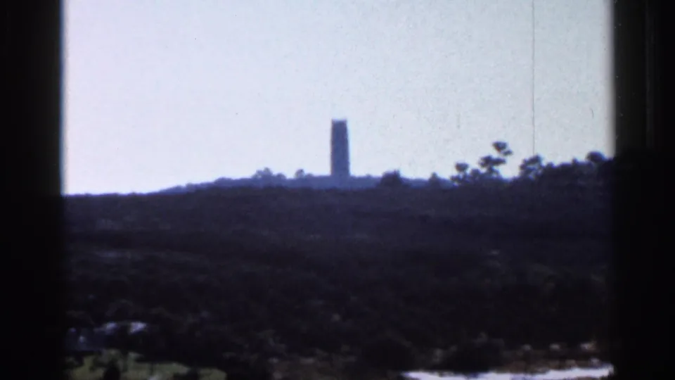 1966 Florida 8mm frame showing a distant slender tower rising above trees, viewed through a dark window frame under a pale sky.