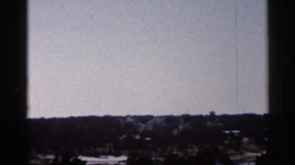 Brief Florida roadside view from the 1966 8mm clip, with tree line and small bright shapes partly hidden by shadow.