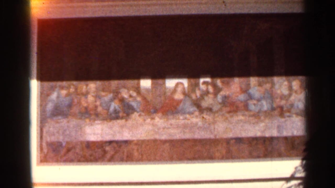 Framed reproduction of The Last Supper seen in a dim room.