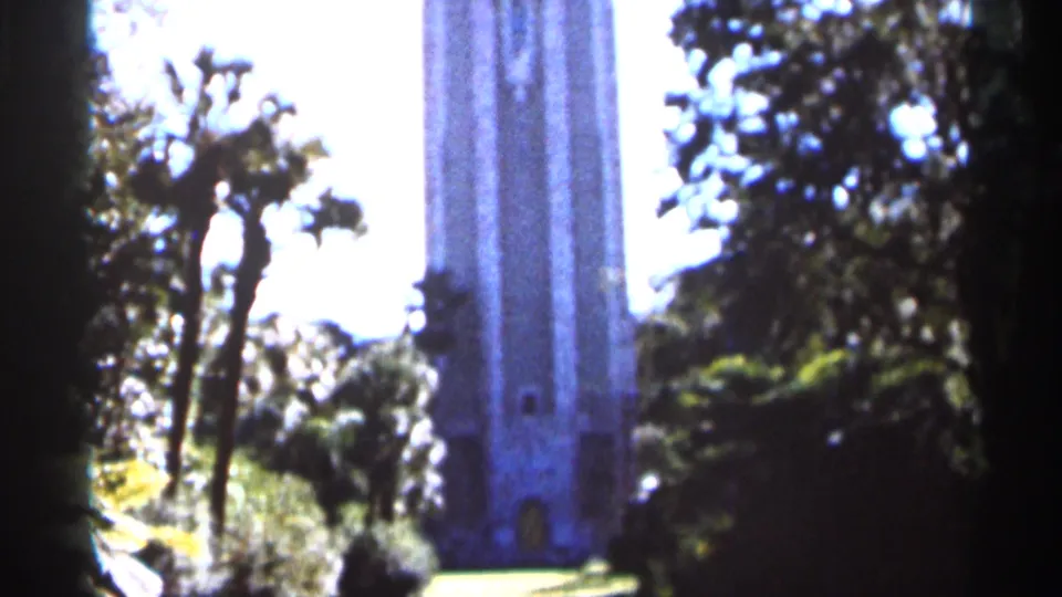 1966 Florida 8mm frame with a tall stone tower behind trimmed palms, leafy trees, and garden-like landscaping.