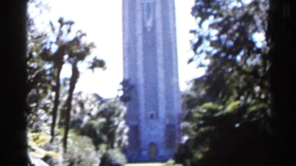 1966 Florida home-movie frame of a tall tower seen through palms and leafy landscaping, with strong exposure and soft focus.