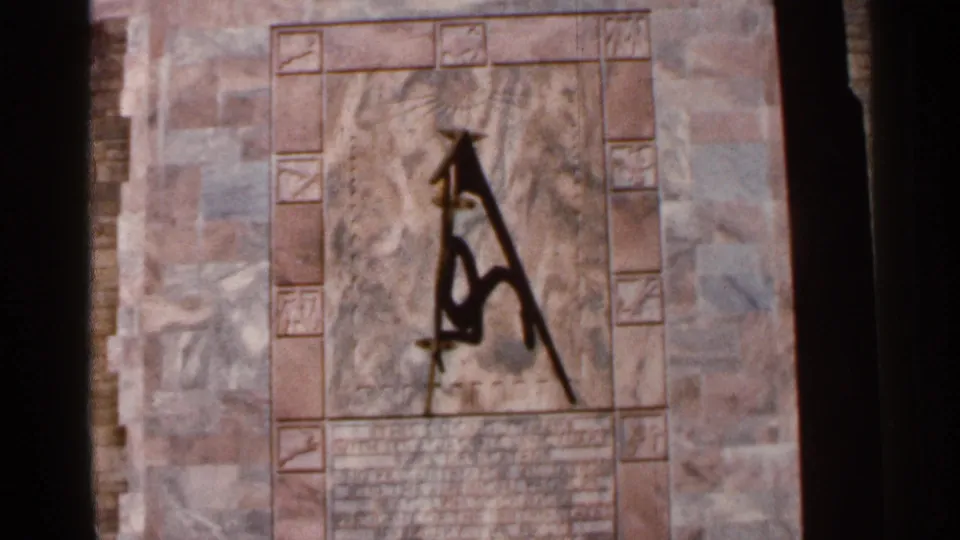 Handheld 8mm view of a dark abstract symbol or mark on patterned stone, with soft focus and warm mid-1960s color.