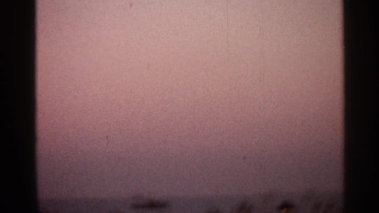 1966 8mm frame with a muted pink sky, low distant horizon, and visible film borders from the sunset sequence.