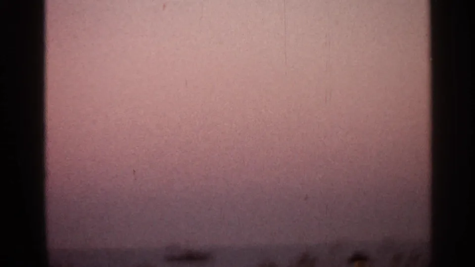 1966 8mm frame with a muted pink sky, low distant horizon, and visible film borders from the sunset sequence.