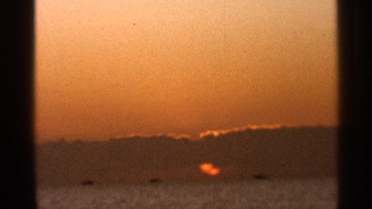 1966 Florida 8mm frame with an orange sun over water, a dark distant shoreline, warm sky, and a vertical gate or frame shadow.