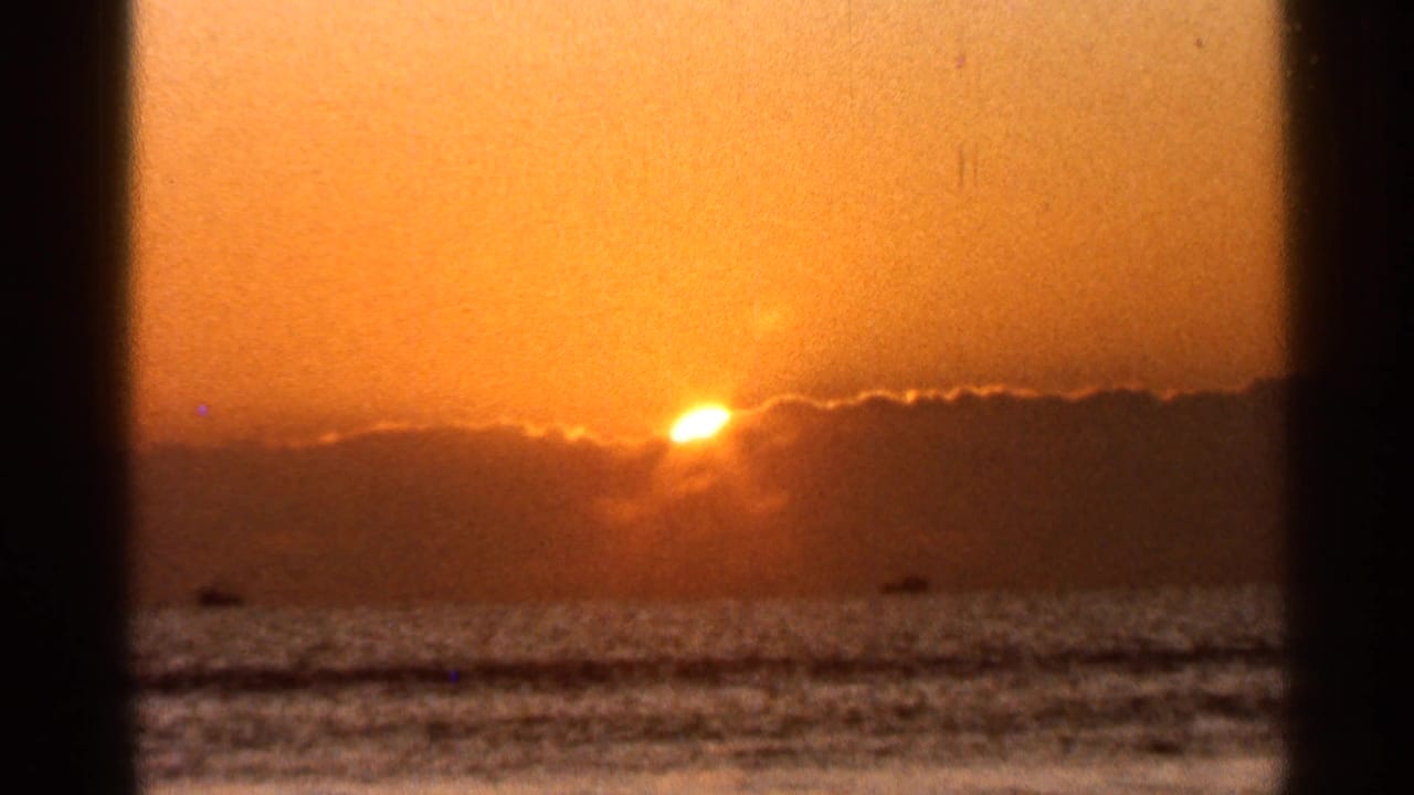 Orange sunset over the ocean with the sun partly behind a cloud bank.