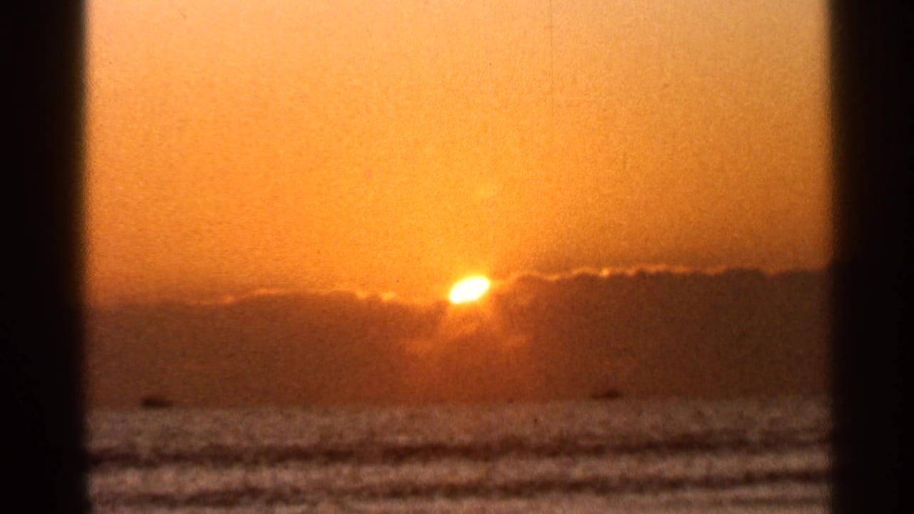 1966 Florida 8mm frame showing orange sunset light, rippled surf, and a dark cloud line along the ocean horizon.