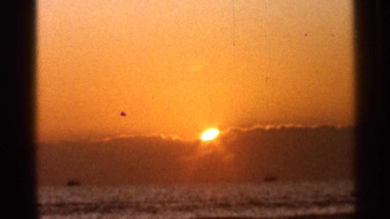 Orange sunset over open water with a dark cloud bank and visible film-frame edges.