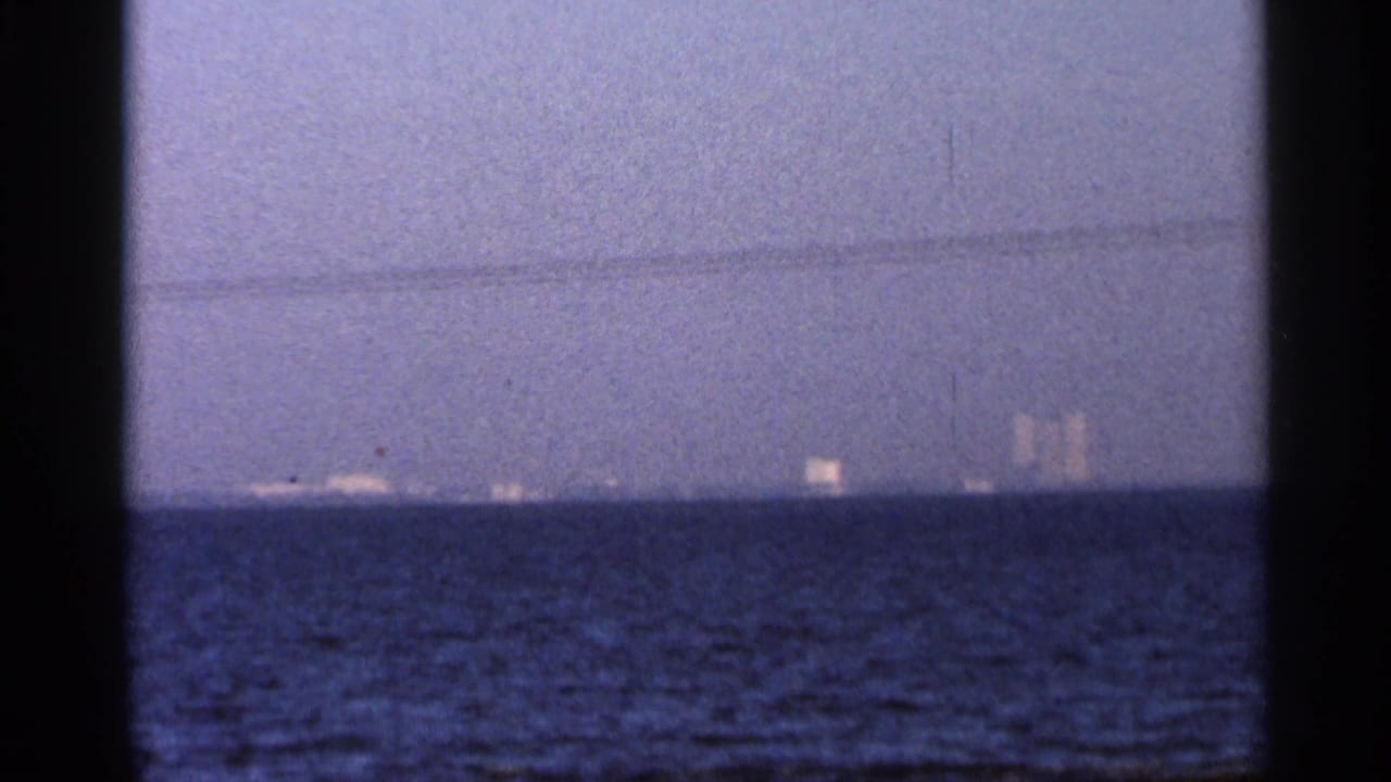 Blue twilight ocean horizon with faint distant lights and vertical silhouettes.