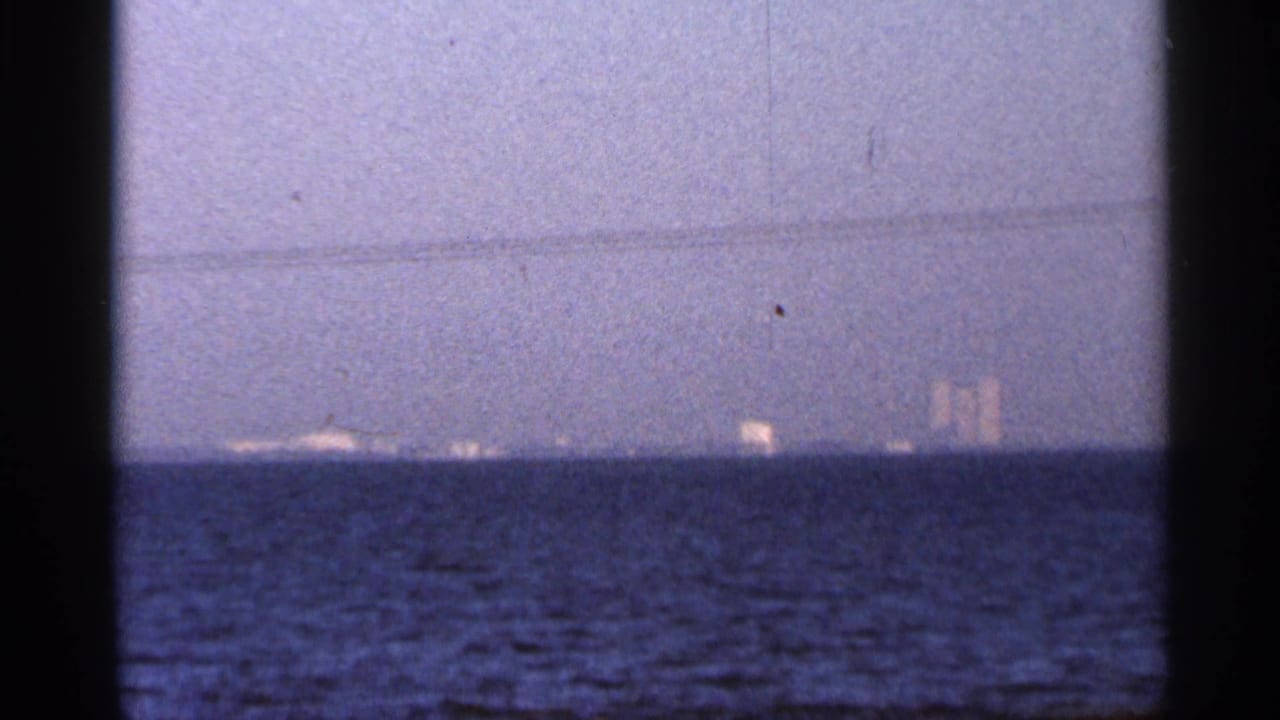 1966 Florida 8mm view across blue water toward small distant lights or shoreline forms at twilight.