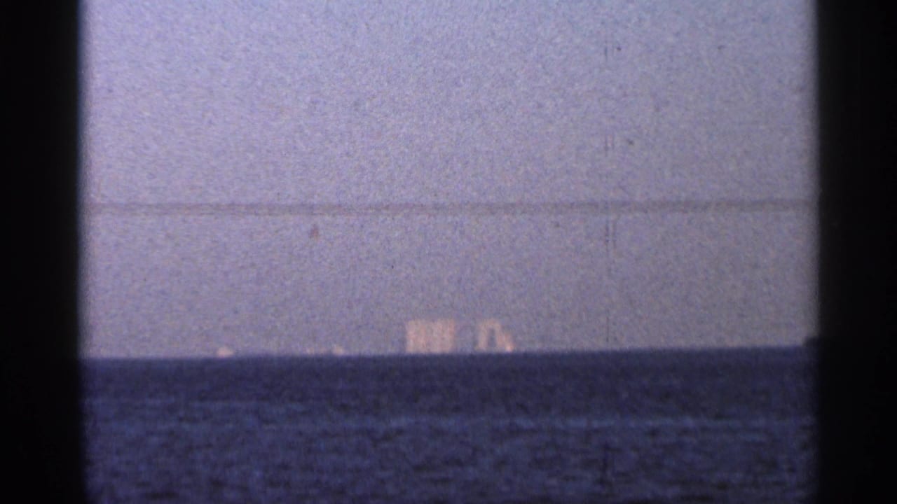 Late 1966 Florida twilight frame showing dark water, a pale horizon, and indistinct distant lights over the sea.