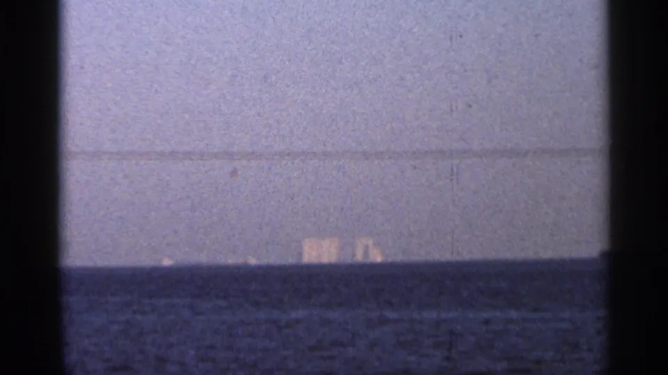 Late 1966 Florida twilight frame showing dark water, a pale horizon, and indistinct distant lights over the sea.