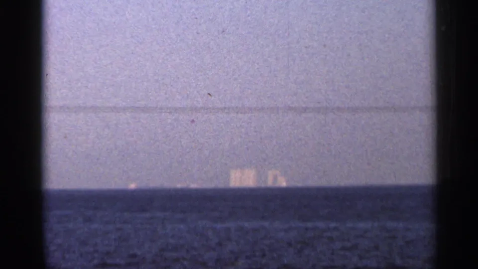 Distant waterfront view in a 1966 Florida home movie, with small structures barely visible beyond the water.