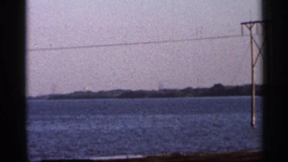 1966 Florida shoreline view across water, with a utility pole and suspended line near the frame edge.