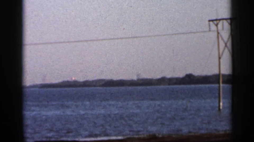 8mm home-movie frame from 1966 Florida showing a distant shoreline, open water, and a utility line at right.