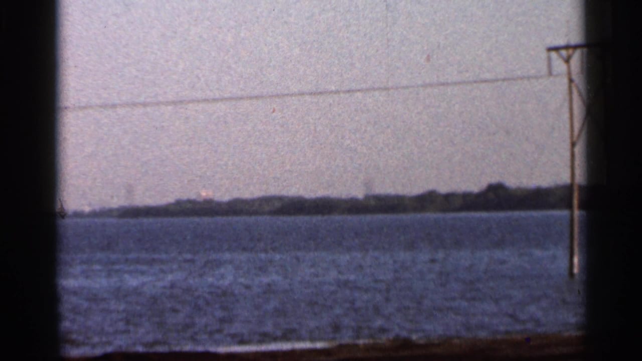 1966 Florida home-movie frame showing a calm river, hazy shoreline, utility pole, and power lines.