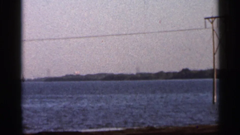 1966 Florida home-movie frame showing a calm river, hazy shoreline, utility pole, and power lines.