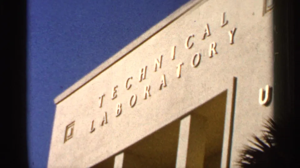 Low-angle 1966 Florida frame of a pale institutional facade with Technical Laboratory lettering against blue sky.