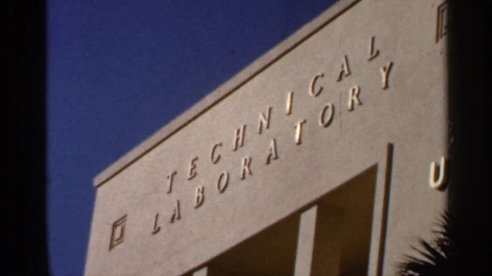 1966 Florida home-movie frame of a Technical Laboratory facade, blue sky, and palm-like foliage at the edge.