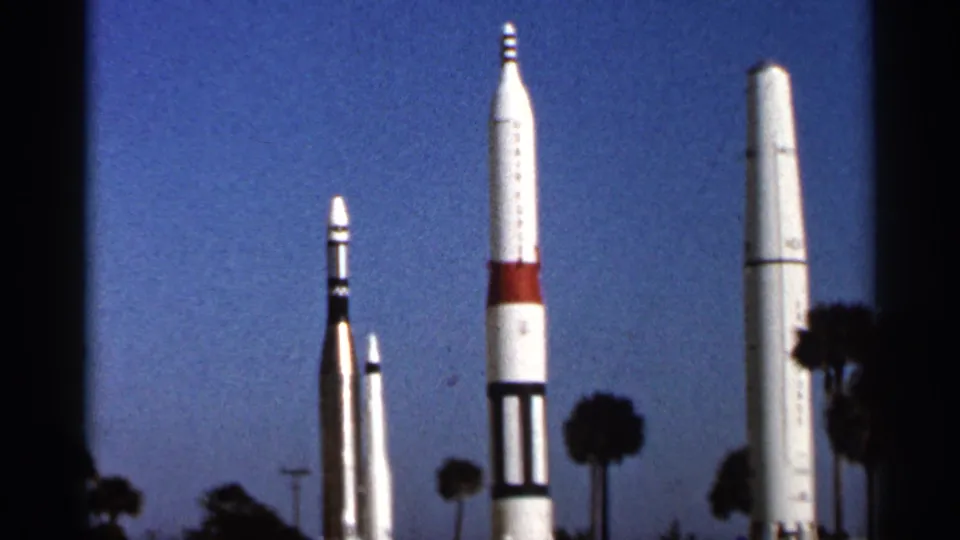 1966 Florida 8mm frame showing multiple upright rocket displays beneath a clear blue sky with palm trees in the background.