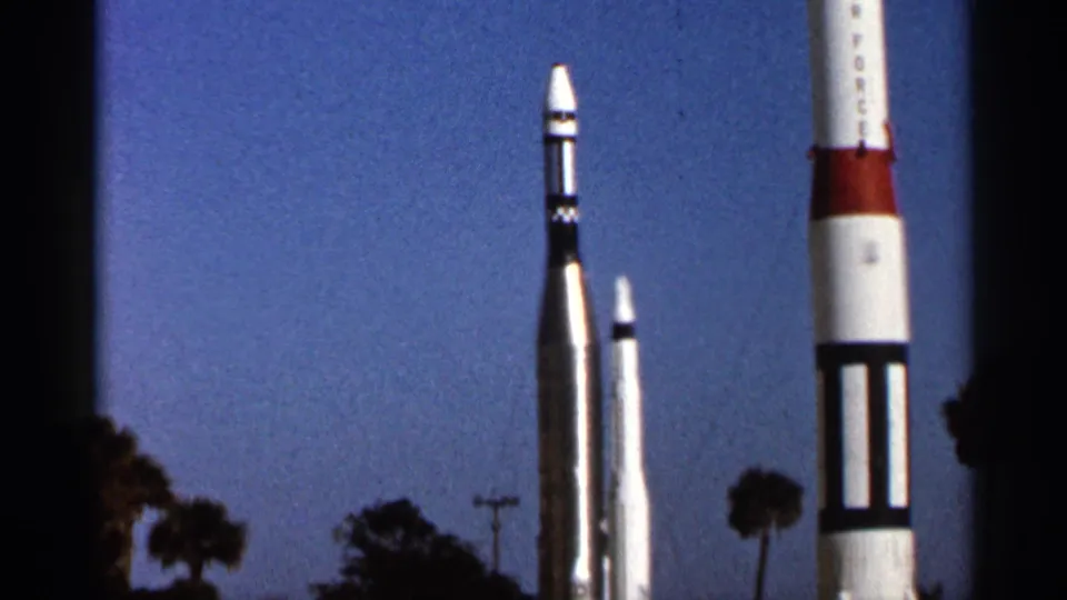 1966 Florida 8mm frame showing rocket displays cropped by the camera, with palm trees and utility poles in the distance.