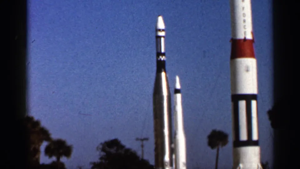 1966 Florida home-movie frame showing several outdoor rocket displays of different sizes with palm trees in the background.