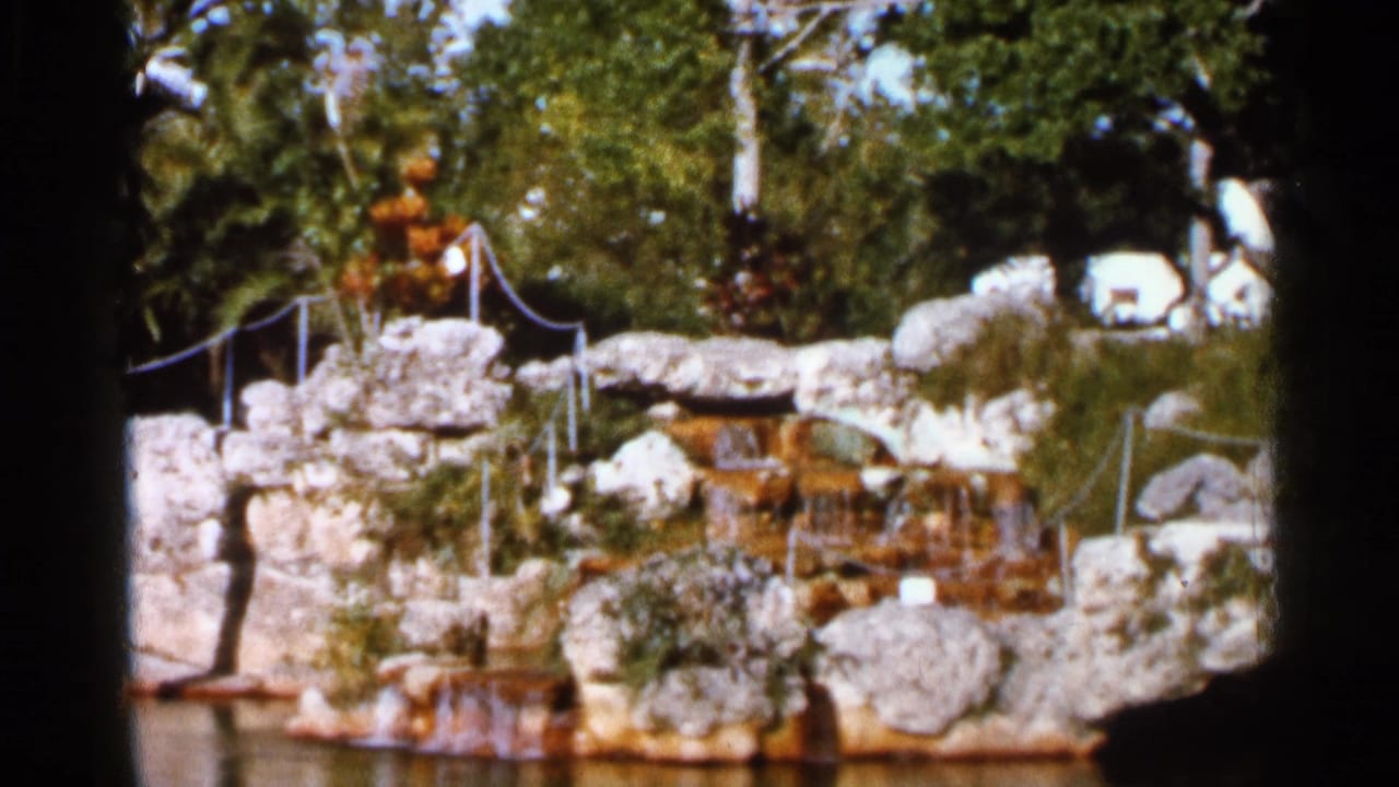 1966 Florida 8mm view of Venetian Pool rockwork, railings, trees, water, and small cascading falls.