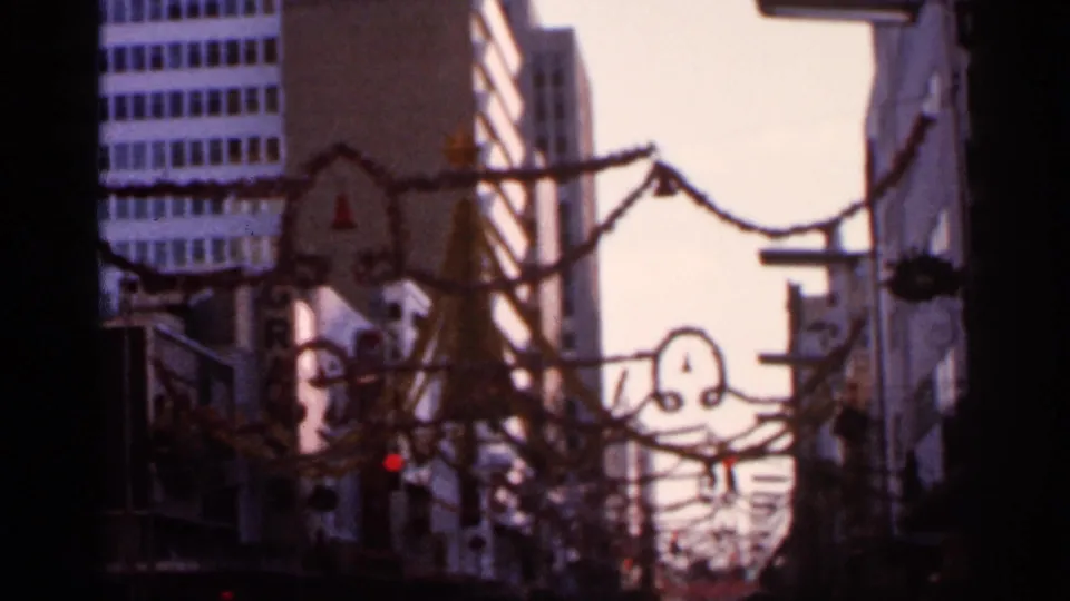 1966 Florida 8mm frame showing a soft, handheld downtown view with garlands and street fixtures overhead.