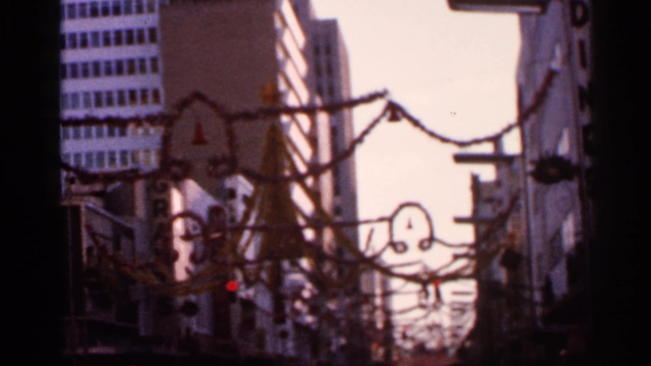 1966 Florida 8mm frame of downtown buildings, garlands, and suspended holiday shapes in warm soft focus.