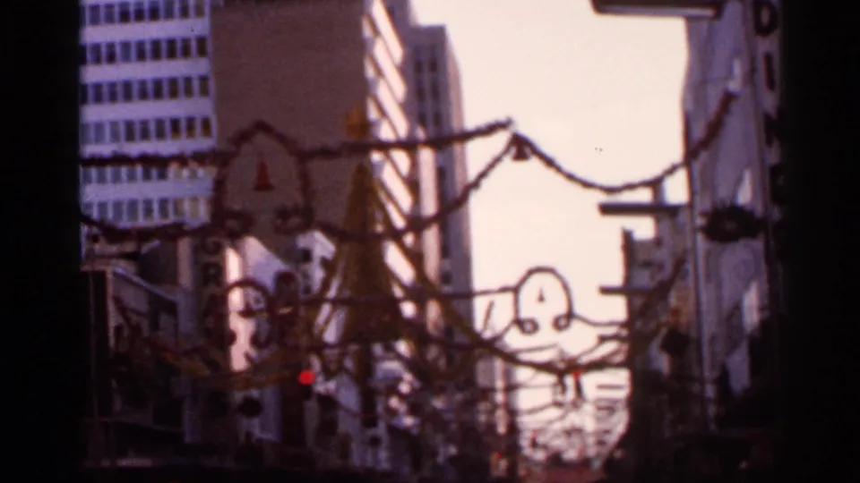 1966 Florida 8mm frame of downtown buildings, garlands, and suspended holiday shapes in warm soft focus.