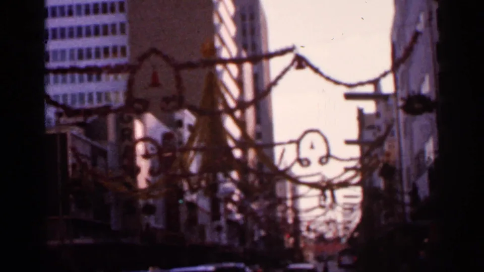 1966 Florida home-movie frame showing a city street with buildings, overhead decorations, and dark film-edge shadowing.