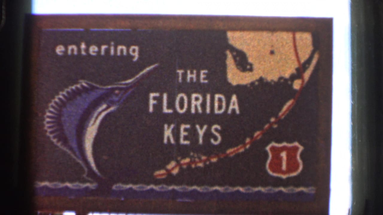 1966 Florida home-movie frame repeating the Florida Keys entry sign, including the marlin graphic, stylized map area, and Route 1 shield.