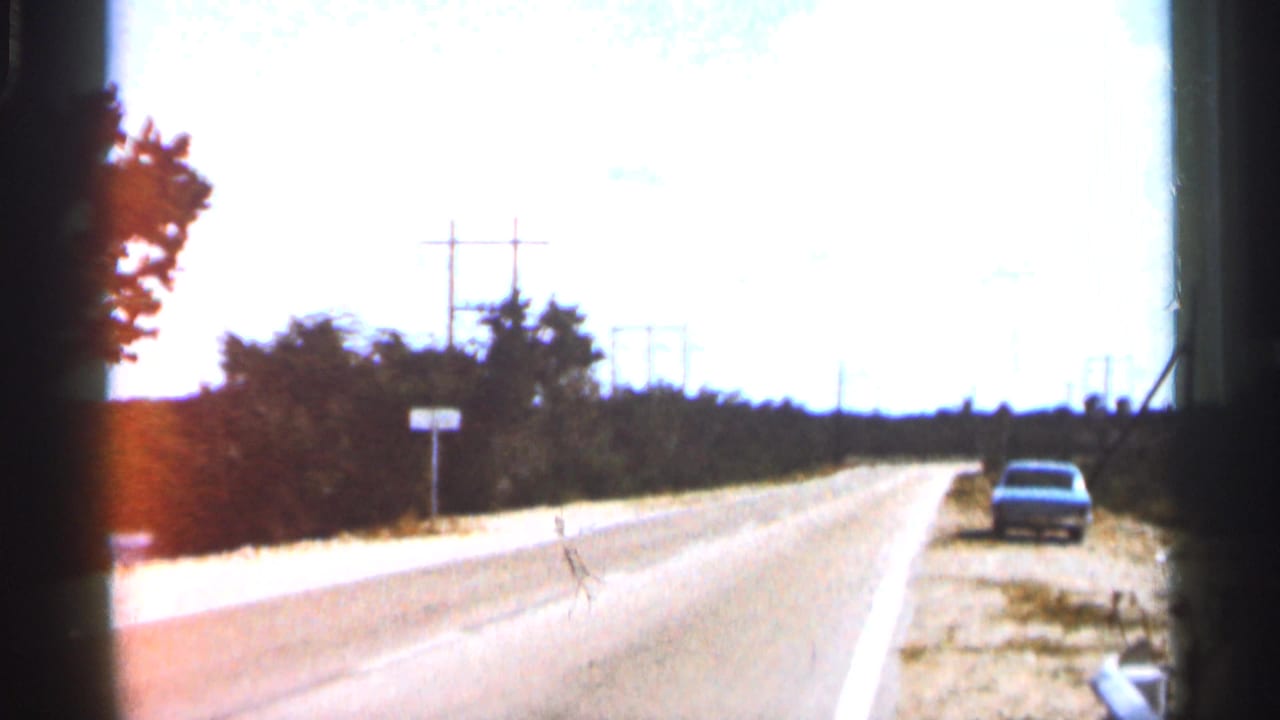 1966 Florida road-trip frame looking down a bright highway toward the distance, with a car near the right shoulder, trees, power poles, and washed sunlight.