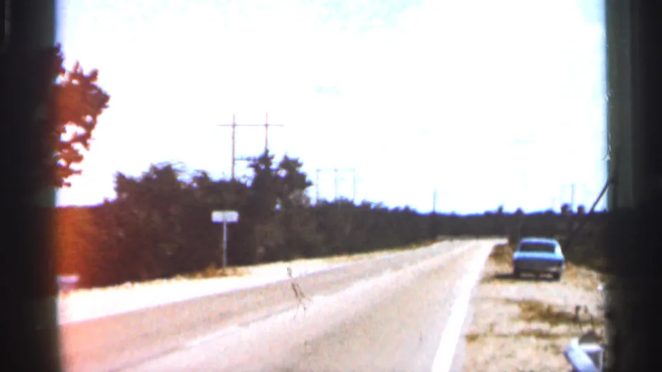 1966 Florida road-trip frame looking down a bright highway toward the distance, with a car near the right shoulder, trees, power poles, and washed sunlight.