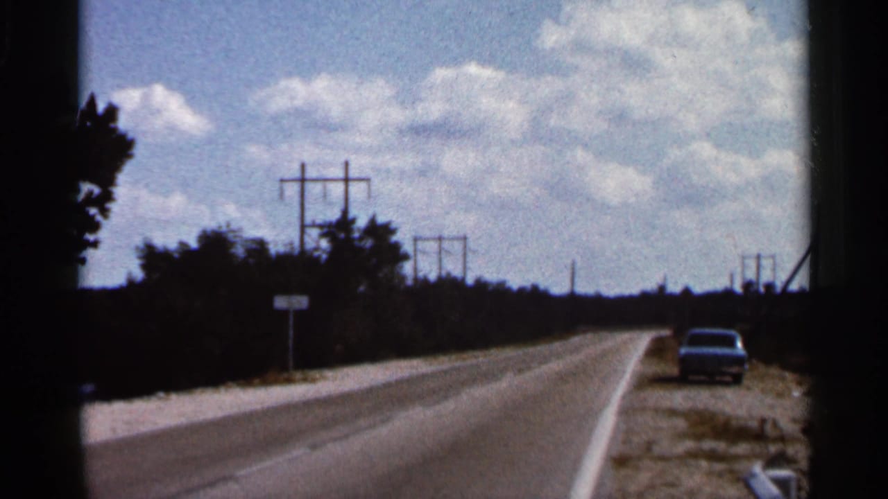 1966 Florida 8mm frame showing a sunny roadside approach with utility poles, trees, and a car on the shoulder.