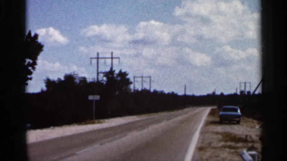 1966 Florida 8mm frame showing a sunny roadside approach with utility poles, trees, and a car on the shoulder.