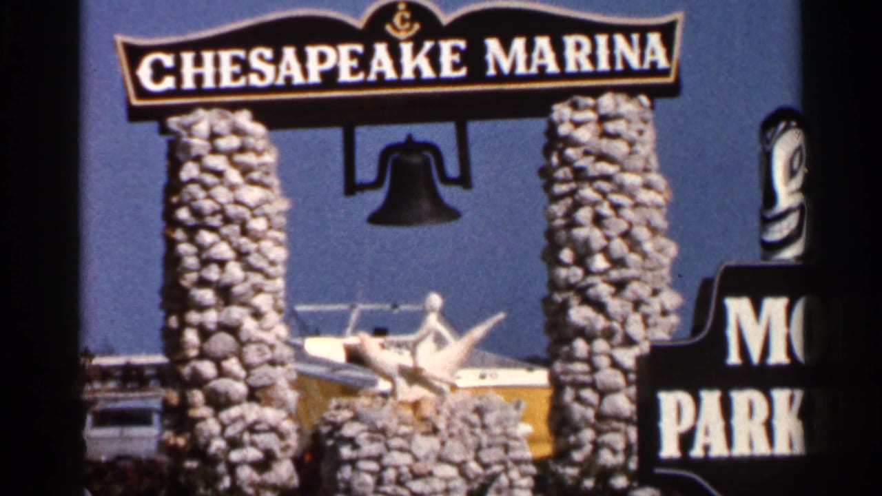 1966 Florida 8mm frame of the Chesapeake Marina sign, stone pillars, hanging bell, boat, and dolphin figure sculpture.