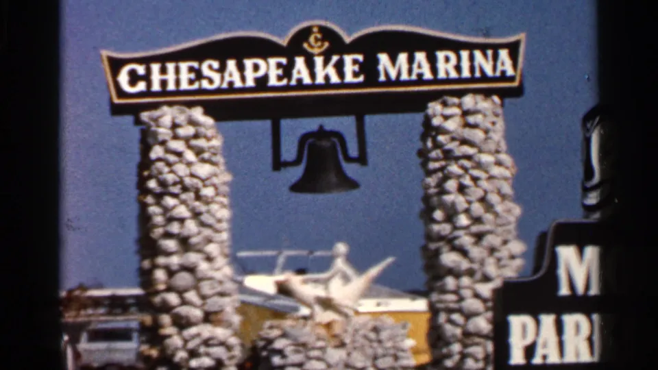 1966 Florida 8mm frame with a closer handheld view of the Chesapeake Marina sign, stone posts, hanging bell, and boat behind.