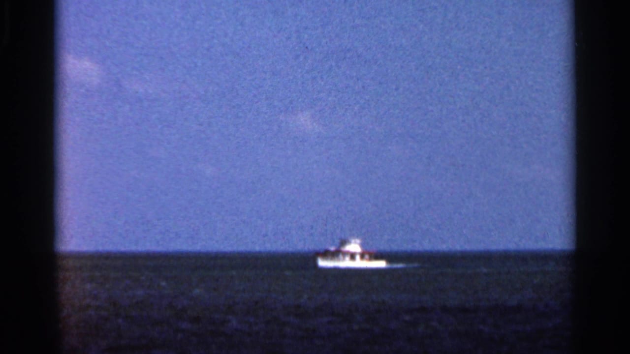 Small white boat on dark ocean water beneath a blue sky.