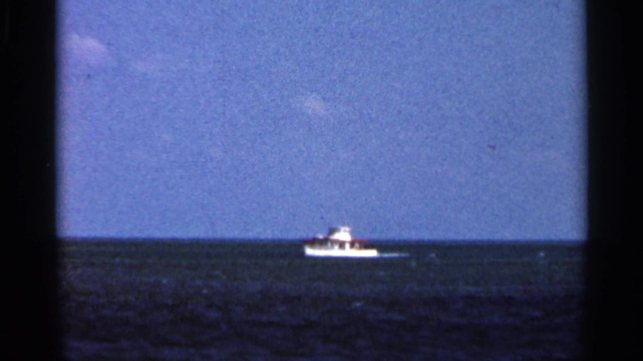 White boat farther right on the ocean horizon under blue sky.