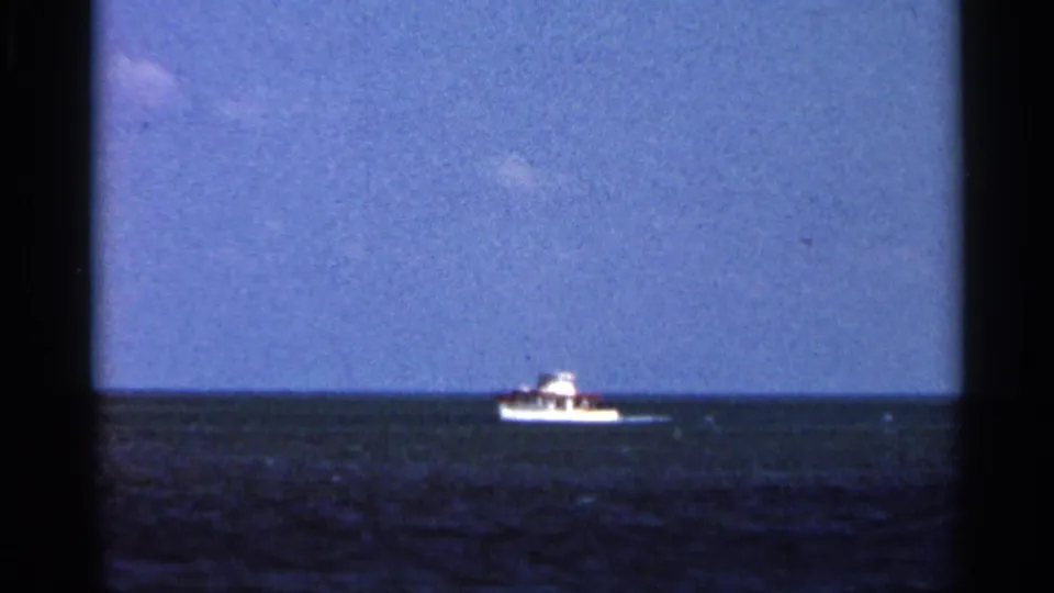 Small white boat with a dark cabin area seen at a distance on calm Florida ocean water, from a 1966 8mm home movie.