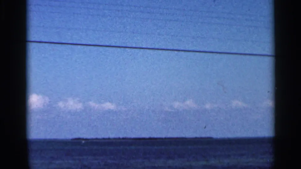 Distant low Florida shoreline across blue ocean water, with pale clouds and a visible 8mm frame border in 1966 footage.