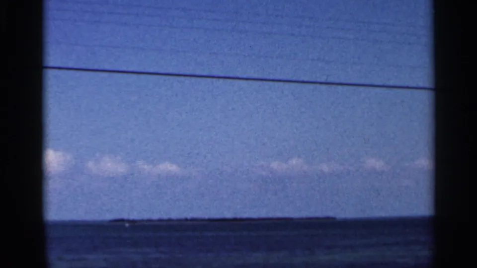 Low coastal land and cloud band seen across Florida ocean water in 1966 home-movie footage, with dark 8mm frame edges.