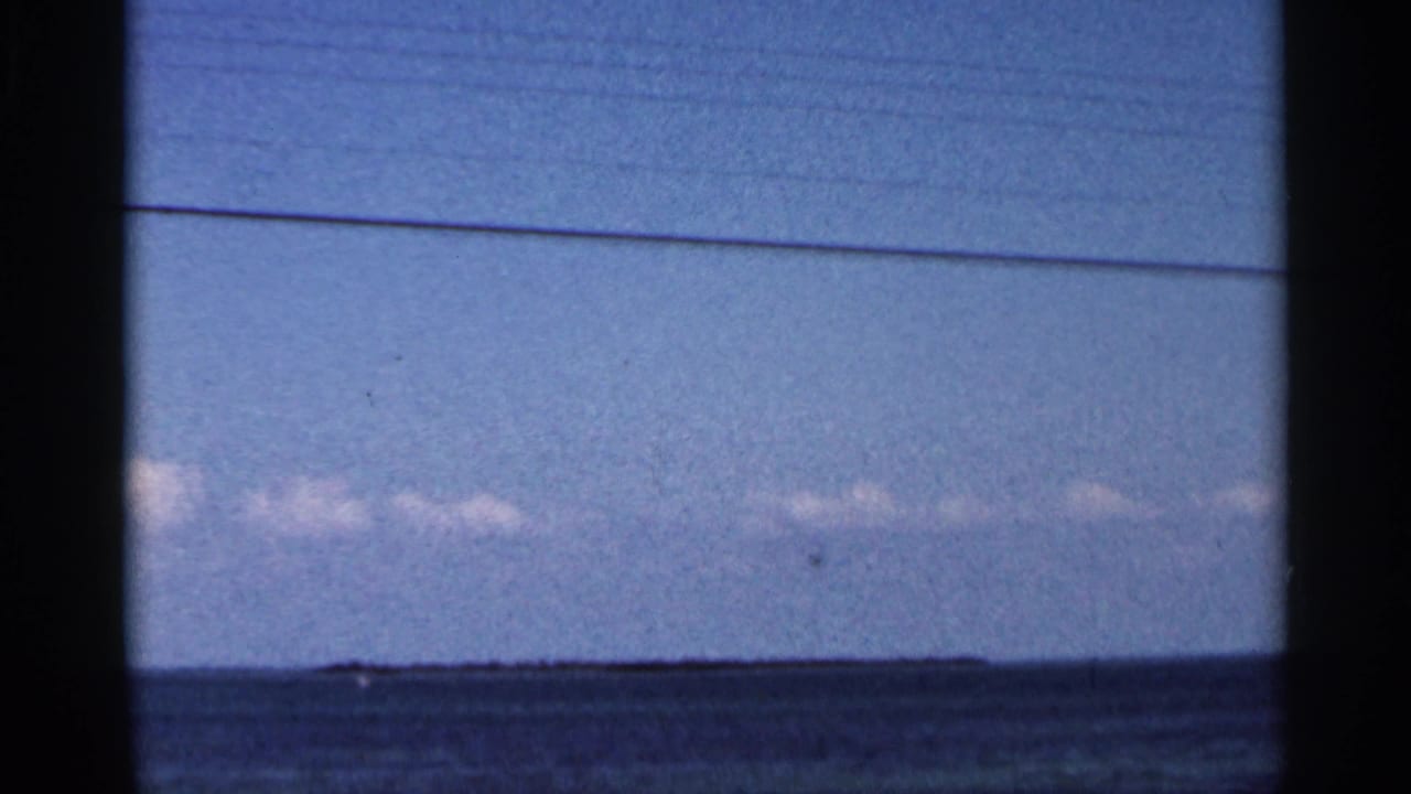 1966 Florida coastal view with blue water, pale sky, low clouds, and a small distant shape near the horizon.