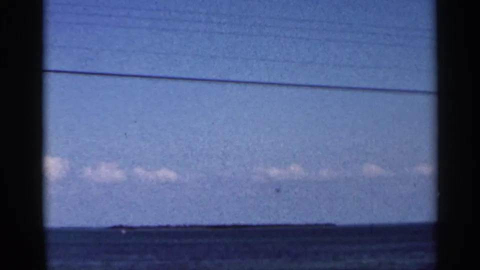 1966 Florida coastal view with blue water, pale sky, low clouds, and a small distant shape near the horizon.