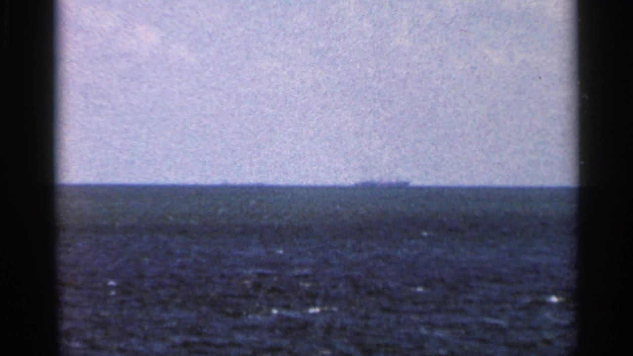 Open water under a pale sky with a low distant landmass on the horizon.