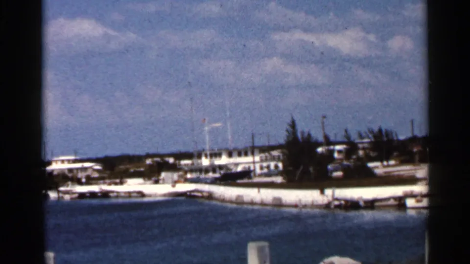 1966 Florida coastal view showing a white shoreline edge, small boats, low buildings, trees, and blue water from a home-movie perspective.